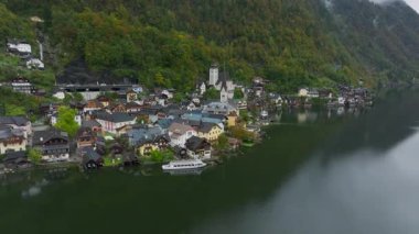 Kamera hareketleri, bulutlu bir gökyüzünün altındaki görkemli dağların çerçevelediği göldeki renkli Hallstatt evlerini yakalar ve köylerin manzaralı güzelliklerini gösterir..