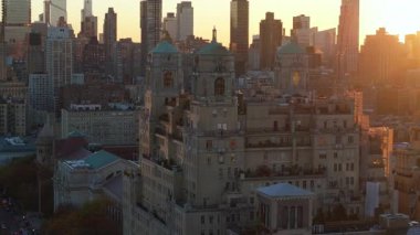 New York 'un batısındaki Central Park boyunca uzanan ikonik Beresford binasının arkasında batan hava manzaralı güneş kentsel ufuk çizgisinin üzerindeki canlı alacakaranlık renklerini vurguluyor..