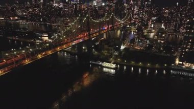 Hava görüntülerinde Queensboro Köprüsü ve Roosevelt Adası gece nefes kesen Manhattan silueti ile birlikte canlı şehir ışıkları ve New York City mimarisini ele geçiriliyor..