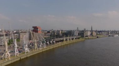 Antwerp, Belçika 'nın canlı şehir manzarası, Scheldt Nehri' ni gözler önüne seriyor. Liman vinçleri ve çarpıcı bir zemin üzerine kurulu kentsel bir siluet..