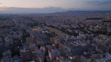 Yunanistan 'ın Selanik kentindeki Egnatia Bulvarı' nda arabalar yol alırken, binalar ve dağlar manzaralı bir zemin oluşturuyor. Sahne, alacakaranlıkta şehrin hareketli atmosferini yansıtıyor..