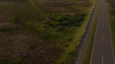 Havadan bakıldığında, Danimarka 'daki Ringkobing Fjord boyunca uzanan sakin bir yol sergilenmekte, bereketli manzaralar ve gün batımında ışıldayan su yansımaları sergilenmektedir..