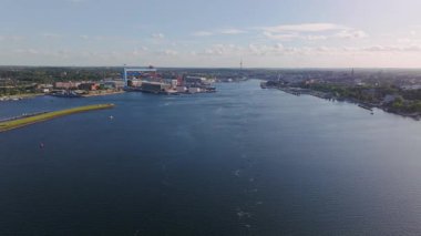 Güneşli bir yaz gününde Kiel Fiyort 'ta kameralar yankılanıyor. Görünüm, arka planında Kiel şehri ve büyük bir konteyner terminali olan limanı gösterir.