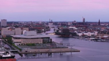 Kopenhag siluetleri modern ve tarihi mimarinin bir karışımını sergiliyor, alacakaranlıkta suya güzel bir şekilde yansıyor, sakin ve resimsel bir şehir manzarası yaratıyor..