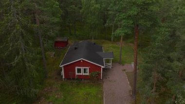 Siyah çatılı kırmızı İsveç evi yemyeşil ormanlarla çevrili bir açıklıkta duruyor. Sakin ortam, yaz boyunca kırsal hayatın güzelliğini gözler önüne seriyor..