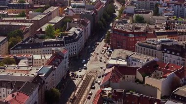 Sarı tramvay Berlin 'de güneşli bir kavşağı geçiyor. Yeşil ağaçlı ve arabalı kırmızı tuğlalı binalar Alman başkentinin güzelliğini gösteriyor..