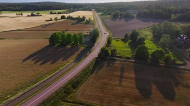 Havadan bakıldığında, Finlandiya 'da yemyeşil tarlalar ve sık ormanlarla çevrili, kırsal bir yol boyunca giden siyah bir araba görülüyor. Sahne huzurlu bir yaz manzarası yakalar..