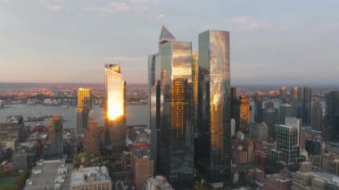 Sıcak akşam ışığı Manhattan şehir merkezindeki modern gökdelenleri yıkıyor, altın saat boyunca cam cephelerde çarpıcı yansımalar yaratarak, kentsel ufuk çizgilerini güzelleştiriyor..