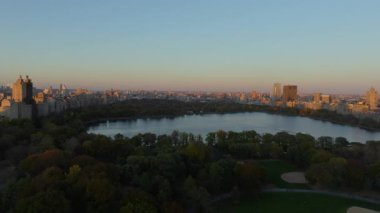 Havadan alınan görüntüler, New York şehrinin silueti tarafından çerçevelenen ve günbatımında sakin bir şehir manzarası yaratan Central Park rezervuarını ve çeşmesini vurguluyor..