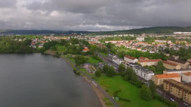 Bulutlu bir günde İsveç 'in bir kasabasında dolaşmak, sakin binalar, dingin bir göl ve yemyeşil alanlar sergiliyor, pitoresk bir şehir manzarası yaratıyor..