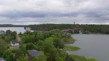 Havadan bakıldığında, Finlandiya 'nın Aland kentindeki küçük adaları birbirine bağlayan bir köprü görülebilir. Sakin sular bulutlu gökyüzünü yansıtırken, eski evler huzurlu manzarayı güzelleştiriyor..