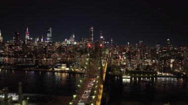 Manhattan şehir merkezindeki aydınlık gökdelenler gece gökyüzüne karşı yükselirken Queens 'ten gelen arabalar ön plandaki Queensboro Köprüsü' ne doğru hızla ilerliyorlar..