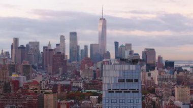 Helikopter perspektifi New York şehrinin ufuk çizgisi üzerinde şafak vakti geri planda Özgürlük Kulesi 'ni yakalıyor, Manhattan' ın canlı kentsel manzarasını ve ikonik mimarisini vurguluyor..