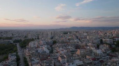 Yunanistan 'ın Selanik kentini kapsayan hava görüntülerinde, gün batımında kentsel mimari ve caddeler sergilenirken, dağlar canlı bir şehir manzarası çerçeveliyor.