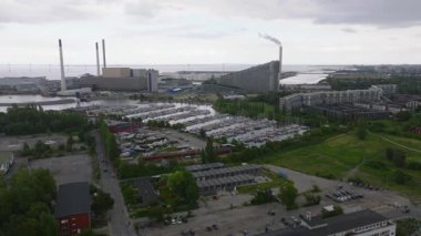 Hava görüntüleri Kopenhag limanını yakalıyor, tekneleri vurguluyor ve enerji santraline Amager Bakke ya da Copenhill atıkları, bulutlu bir yaz gökyüzüne duman bulutu salıyor..