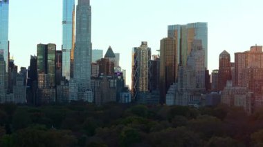 Güneş ışığı, Manhattan şehir merkezinin arkasında batarken gökdelenlerden yansıyor. Central Park 'ın sonbahar ağaçları ve kentsel güzelliklerle çevrili muhteşem bir manzarası var..