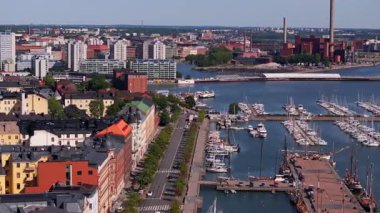 Helsinki limanını tekneler ve turistlerle canlı olarak gösteren hava görüntüleri var. Yerliler parlak bir gökyüzü altında büyüleyici bir yaz ortamı yaratarak şehrin tadını çıkarıyorlar..