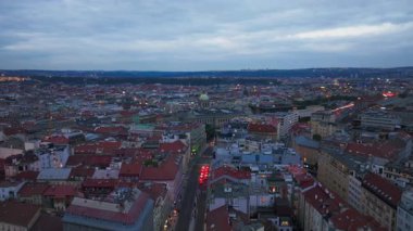 Hava manzaraları Prag şehir merkezini alacakaranlıkta gösteriyor, akan trafiği ve parıldayan şehir ışıklarıyla aydınlatılan canlı bir şehir manzarasını vurguluyor..
