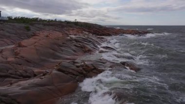 Turkuaz okyanus dalgaları Finlandiya 'nın Aland kentinde kayalık bir sahil şeridine çarpar. Dalgalar kıyıya vurduğunda beyaz deniz köpüğü havaya karışır..
