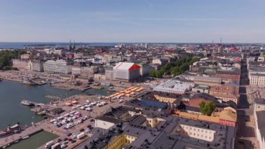 Hava manzaraları Helsinki 'nin canlı şehir merkezini vurguluyor, hareketli Pazar Meydanı' nı, Uspenski Katedrali 'ni ve güneşli bir gökyüzünün altında kabarık bulutlarla birlikte manzaralı Baltık Denizi' ni gösteriyor..