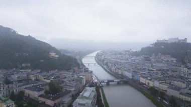 Kamera Avusturya 'nın Salzburg şehrinde ilerliyor. Salzach Nehri şehir merkezine doğru akıyor. Sağda Hohensalzburg Kalesi var..