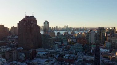 Manhattan gökdelenleri sıcak altın ışıkla parıldıyor, Doğu Nehri suları akşam günbatımını yansıtıyor, şehir manzarası yüksek görüş açısına sahip ikonik şehir manzarasını gözler önüne seriyor..