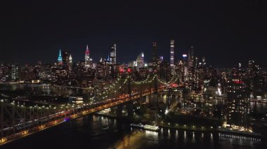 Aydınlatılmış Queensboro Köprüsü ve New York şehrinin gökyüzü manzarası gece Queens ve Manhattan ilçeleri arasında East River 'ı yansıtan parlak ışıkları vurguluyor..