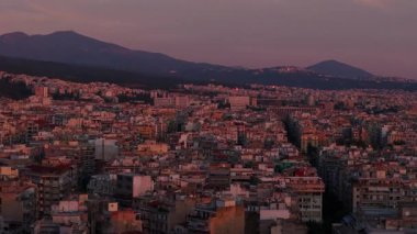 Yunanistan 'ın Selanik kenti, uzak dağlara doğru uzanan kentsel genişliğini gösteriyor. Günbatımının ılık renkleri canlı şehri aydınlatır..