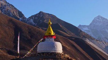 Sıcak güneş ışığı manzarası görkemli Everest Dağı 'nı aydınlatıyor, Dingboche' da canlı dua bayraklarıyla süslenmiş barışçıl Budist stupasının arkasında yükseliyor..