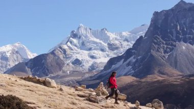 Trekker, Everest Ana Kampı yakınlarındaki engebeli dağ patikalarında Himalaya zirveleri ve dua bayraklarıyla kayalık arazide geziniyor..