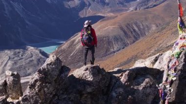 Dağ tırmanışçısının canlı kırmızı ceketi ve dolu sırt çantasıyla Nangkarshang Tepesi 'nin tepesinde karlı sıradağların arasında durduğu hava manzarası..