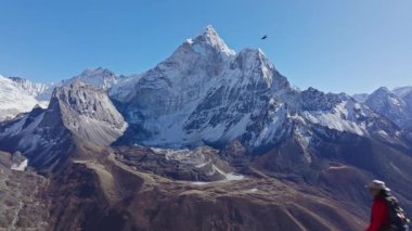 Nangkarshang Tepesi 'nde zaferle ayakta duran dağcı, Ama Dablam dağının arkasında yükseliyor, tırmanma başarısını ve dağlık yaban hayatını ifade ediyor..