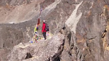 Kırmızı ceketli ve sırt çantalı dağcı kayalık arazide duruyor, Himalaya 'nın görkemli Nepal manzarasıyla kaplı tepelerine bakıyor..