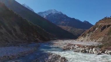Himalaya nehrinin kıvrımları kayalık araziyi oyuyor, çiğ, el değmemiş Nepal dağ manzarasına karşı karla kaplı tepeleri ortaya çıkarıyor..