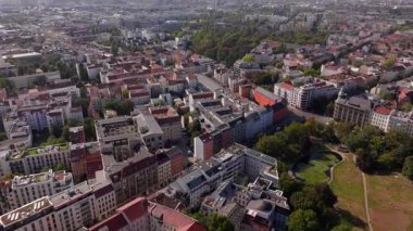 Berlin 'deki binaların üzerinde çalışan bir vinç görülüyor. Arabalar kırmızı kökler altında cadde boyunca sürüyorlar..