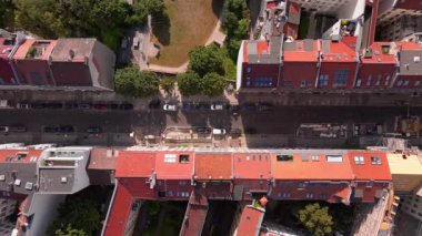 Tipik bir Berlin mahallesinin parkı, binalarda güneş panelleri, sokakta park etmiş arabalar ve kaldırımda yürüyen insanlar..