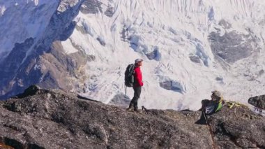 Dağcı kırmızı ceketli kayalık yamaçta, Everestler yakınlarındaki görkemli Himalaya manzarasına bakıyor..