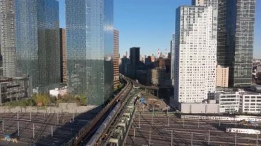 Metro treni, yükseltilmiş raylar, New York silueti ışıldıyor, güneş ışığı şehir ulaşımı altyapısını havadan aydınlatıyor..