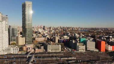 Long Island City, Queens 'teki cam gökdelen cephesinde parlayan güneş ışığı, öğle vakti şehir manzarası sırasında geniş tren istasyonu üzerinde Manhattan gökdeleni olduğunu gösteriyor..