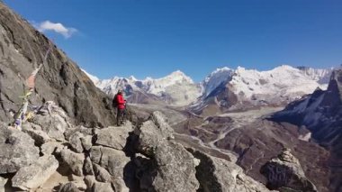 Dağcı Everest Dağı 'nın yakınındaki kayalık yolda ilerliyor. Dalgalanan renkli dua bayrakları, engebeli araziyi ve Himalaya dağcılık deneyiminin ruhani özünü ele geçiriyor..