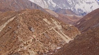 Dağcılık grubunun, Himalayalar 'ın yüksek kar zirveleriyle çevrili Everest Dağı' nın ana kampı yakınlarındaki kayalık patikada yürüyüş görüntüsü..