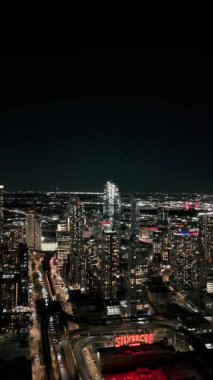 Dikey format, New York, Queens borough 'da gece vakti Long Island City siluetini yakalar. Parlak şehir ışıkları gökdelenleri aydınlatır, canlı şehir manzarasını gözler önüne serer.
