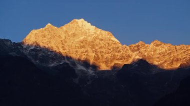 Güneşin doğuşuyla parlayan dağ zirvesi, karlı Everest zirvesini aydınlatan altın ışınlar, aşağıdaki sarp kayalık manzaralar, havadan bakıldığında..