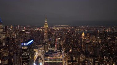 Gece vakti gökyüzü, Manhattan şehir merkezinin parlayan siluetini, Empire State binasının aydınlık sokakların üzerinde yükseldiğini ve yükselen mimari siluetleri gözler önüne seriyor..