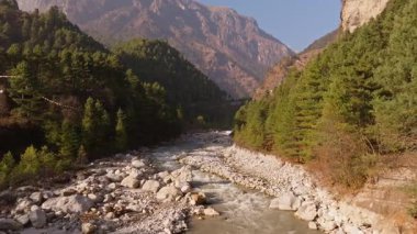 Kristal berrak su, kayalarla dolu ve yemyeşil ağaçlarla çevrili bir vadiden akar. Nepal 'deki Everest Dağı' nın arka planında görkemli Himalayalar bulunur..
