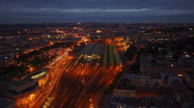 Prag ana tren istasyonunun hava manzarası alacakaranlıkta parlayan gölgelikleriyle, arabalar ve tren rayları istasyonun etrafını sararken.