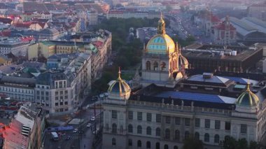 Prag Ulusal Müzesi 'nin altın saatinde gün batımında parlayan kubbesinin hava manzarası. Arabalar geçiyor ve arka planda ana tren istasyonu var..