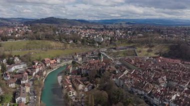 Havadan bakıldığında tarihi Bern şehri, ortaçağ eski kasabası ve kıvrımlı Aare nehri boyunca uzanan yeşil alanlar yumuşak bahar bulutlarının altında..