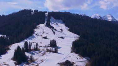 Gstaad yakınlarında orman boyunca kıvrılan karlı kayak yamaçları arka planda muhteşem İsviçre Alplerini gözler önüne seriyor..