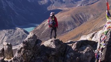 Dağ tırmanışçısının canlı kırmızı ceketi ve dolu sırt çantasıyla Nangkarshang Tepesi 'nin tepesinde karlı sıradağların arasında durduğu hava manzarası..